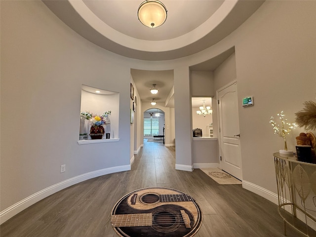 hall with hardwood / wood-style floors, a raised ceiling, and a notable chandelier