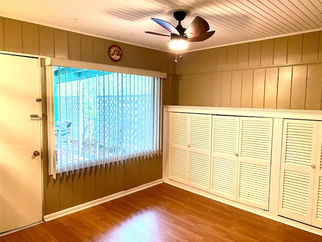 unfurnished bedroom featuring wooden walls, hardwood / wood-style flooring, ceiling fan, ornamental molding, and a closet