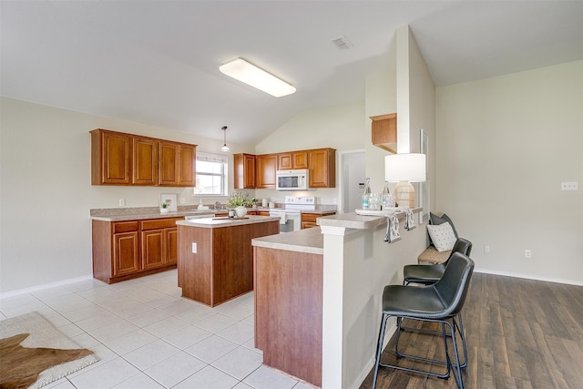 kitchen with kitchen peninsula, pendant lighting, vaulted ceiling, a breakfast bar, and white appliances