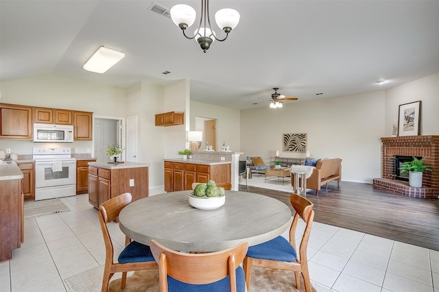 dining area with a brick fireplace, ceiling fan with notable chandelier, light hardwood / wood-style flooring, and lofted ceiling