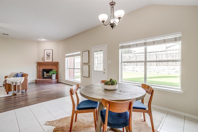 dining room featuring a brick fireplace, light hardwood / wood-style floors, lofted ceiling, and a healthy amount of sunlight