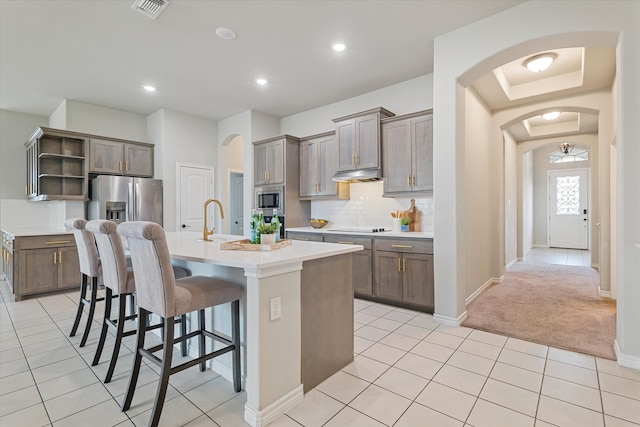 kitchen with a kitchen island with sink, light carpet, backsplash, a breakfast bar, and appliances with stainless steel finishes