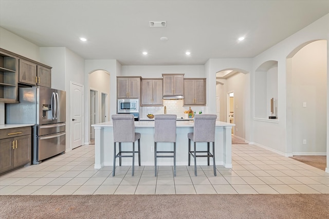 kitchen with light colored carpet, appliances with stainless steel finishes, a breakfast bar, and a center island with sink