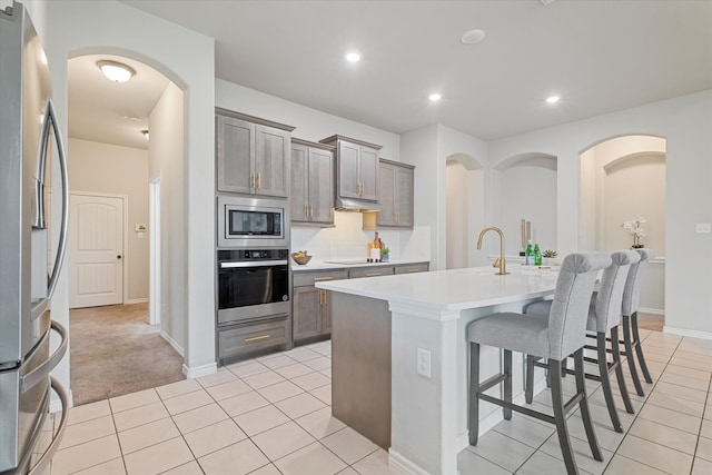 kitchen featuring an island with sink, a kitchen breakfast bar, stainless steel appliances, decorative backsplash, and light tile patterned floors