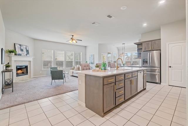 kitchen featuring appliances with stainless steel finishes, sink, a tile fireplace, hanging light fixtures, and a center island with sink