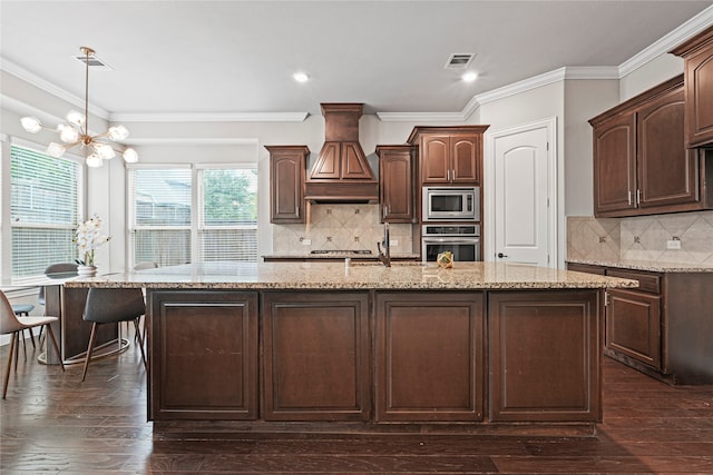 kitchen with a kitchen island with sink, a notable chandelier, dark brown cabinetry, appliances with stainless steel finishes, and dark hardwood / wood-style flooring