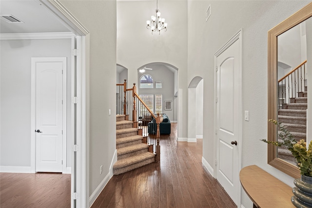 foyer featuring a towering ceiling, crown molding, dark hardwood / wood-style floors, and a notable chandelier