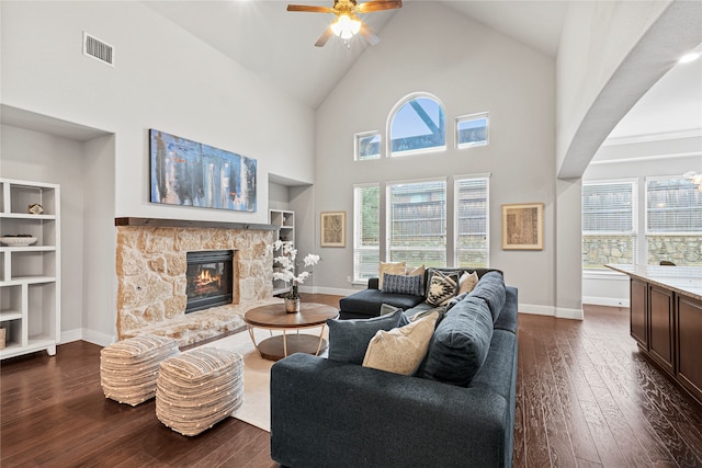 living room with dark wood-type flooring, a stone fireplace, high vaulted ceiling, and ceiling fan