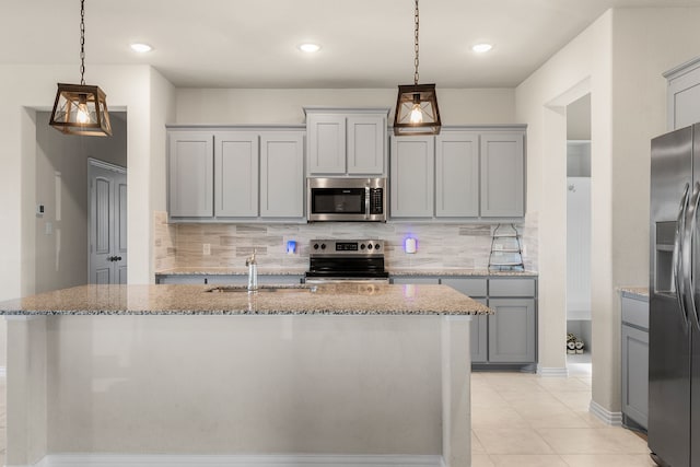 kitchen with stainless steel appliances, light stone countertops, decorative light fixtures, backsplash, and a kitchen island with sink