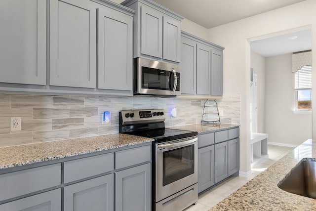 kitchen with gray cabinets, decorative backsplash, light stone counters, and appliances with stainless steel finishes