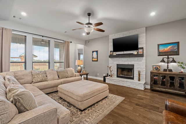 living room featuring a stone fireplace, ceiling fan, and dark wood-type flooring