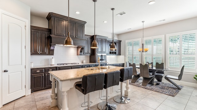 kitchen featuring sink, light stone countertops, a breakfast bar area, an island with sink, and hanging light fixtures