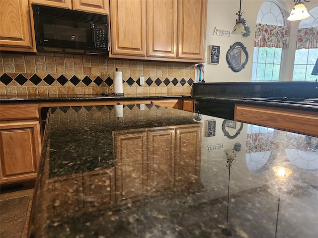 kitchen featuring dark stone countertops, tasteful backsplash, black appliances, and pendant lighting