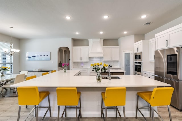 kitchen with a large island, appliances with stainless steel finishes, custom range hood, a breakfast bar, and sink