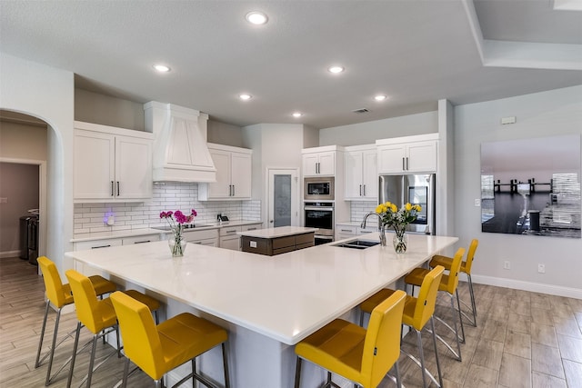 kitchen with stainless steel appliances, a sink, white cabinets, a large island, and custom exhaust hood