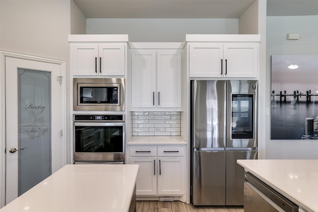 kitchen featuring decorative backsplash, stainless steel appliances, light countertops, light wood-style floors, and white cabinetry