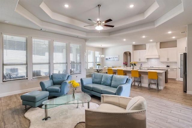 living room with ceiling fan with notable chandelier and a tray ceiling