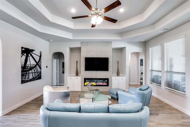 living area featuring light wood-type flooring, a fireplace, arched walkways, and a tray ceiling