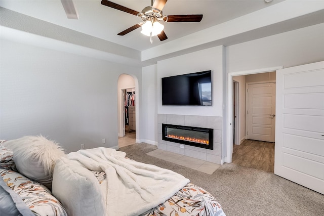 bedroom with a walk in closet, light carpet, a closet, ceiling fan, and a tile fireplace