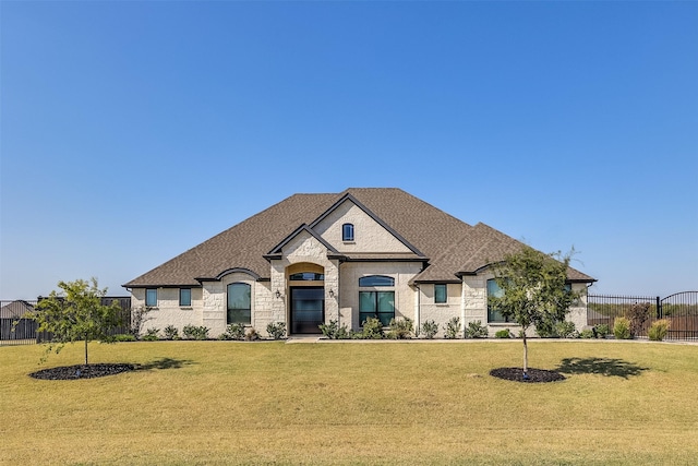 french country home featuring fence, a front lawn, and roof with shingles