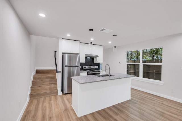 kitchen with light stone countertops, appliances with stainless steel finishes, a center island with sink, decorative light fixtures, and white cabinetry