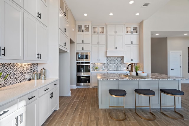 kitchen with white cabinetry, light stone countertops, a breakfast bar, and a center island with sink