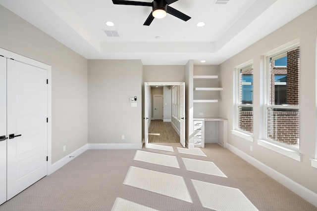 unfurnished bedroom featuring a raised ceiling, light carpet, and ceiling fan