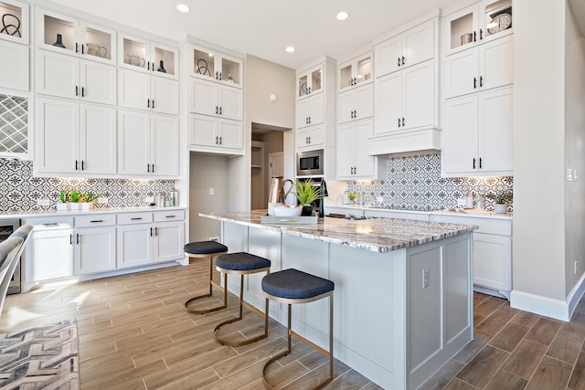 kitchen featuring white cabinetry, backsplash, stainless steel microwave, and a kitchen island with sink