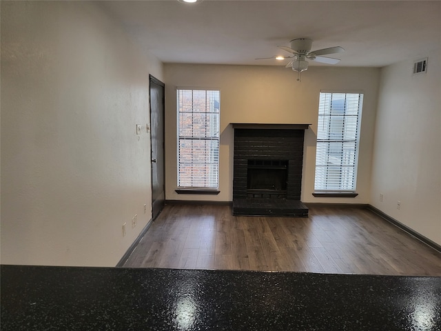 unfurnished living room featuring a brick fireplace, hardwood / wood-style flooring, and ceiling fan