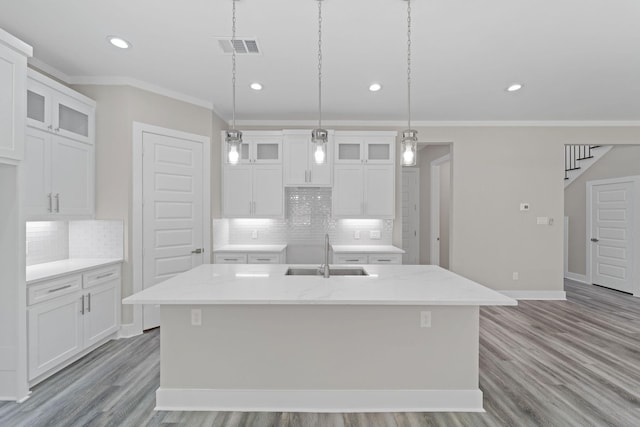 kitchen featuring pendant lighting, sink, crown molding, white cabinetry, and a center island with sink