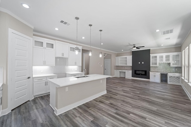 kitchen featuring sink, a large fireplace, an island with sink, white cabinets, and decorative light fixtures