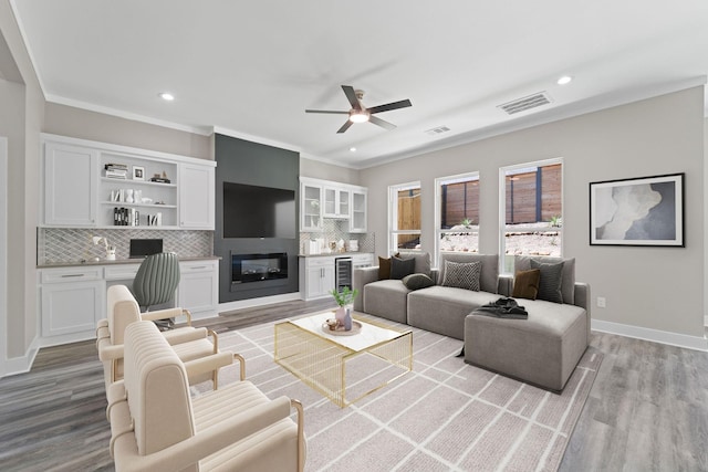 living room featuring light hardwood / wood-style flooring, ornamental molding, beverage cooler, ceiling fan, and a fireplace