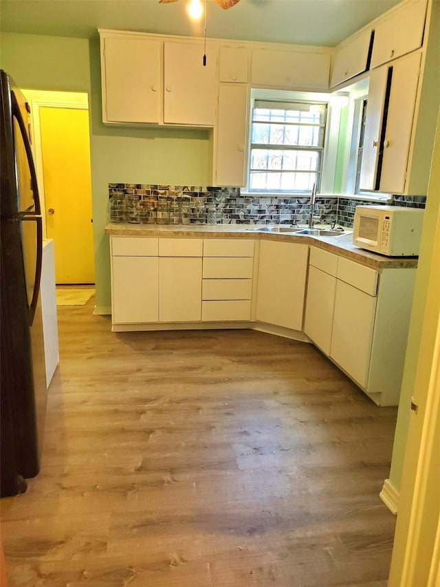 kitchen featuring ceiling fan, sink, black fridge, light hardwood / wood-style floors, and decorative backsplash