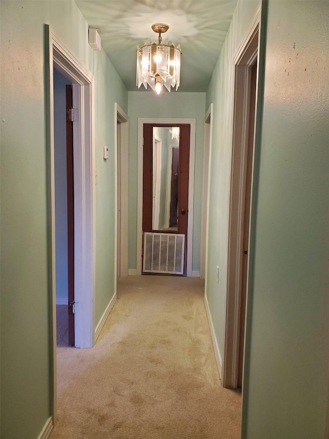 hallway featuring light carpet and a notable chandelier