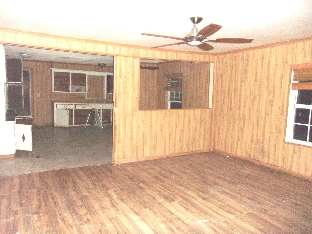 unfurnished room with hardwood / wood-style floors, crown molding, wooden walls, and ceiling fan