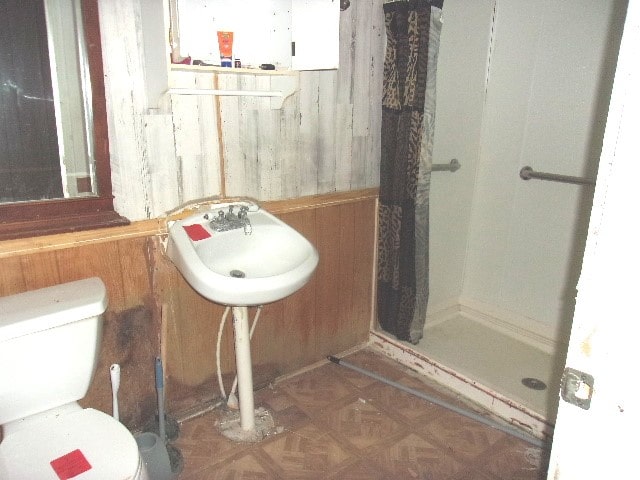 bathroom with parquet floors, wooden walls, toilet, and walk in shower