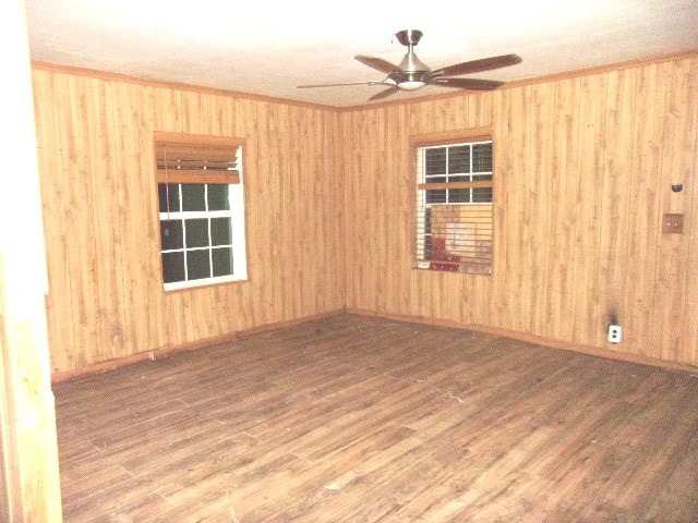 empty room with hardwood / wood-style flooring, wooden walls, and ceiling fan