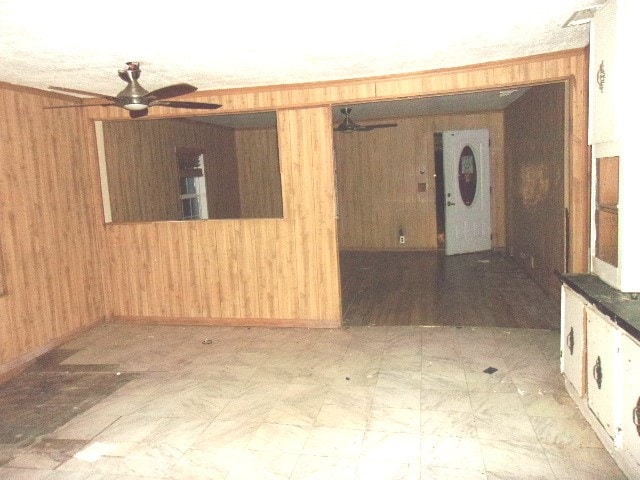 empty room with ornamental molding, ceiling fan, and wood walls