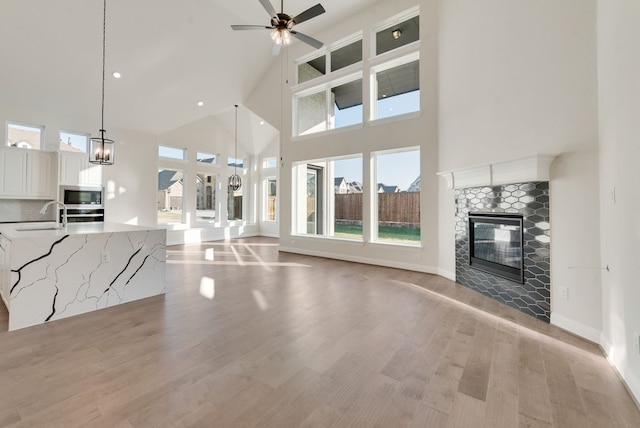 unfurnished living room featuring a ceiling fan, light wood-type flooring, a fireplace, a sink, and recessed lighting