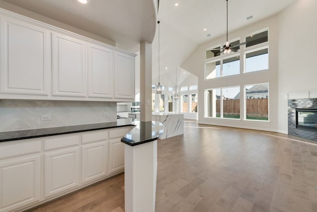 kitchen featuring white cabinets, backsplash, hanging light fixtures, and a multi sided fireplace