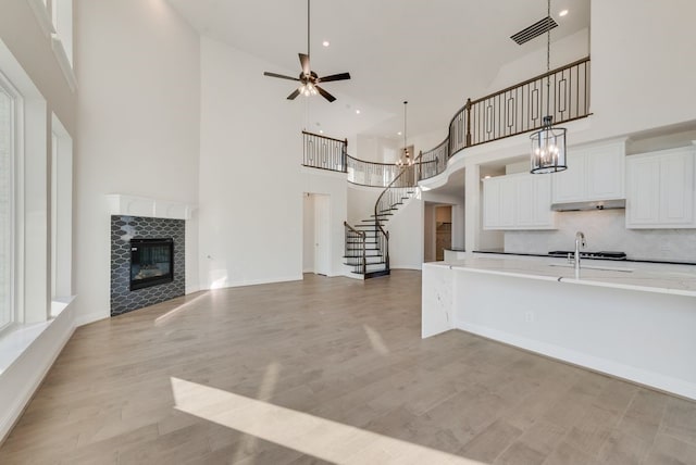 kitchen featuring a high ceiling, white cabinets, hanging light fixtures, ceiling fan, and a fireplace