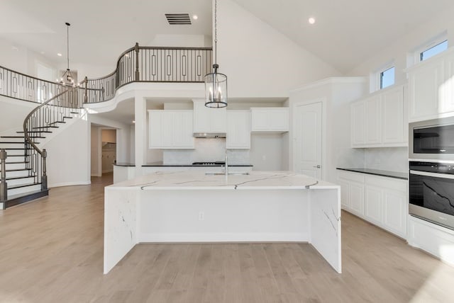 kitchen with decorative light fixtures, a large island with sink, high vaulted ceiling, and dark stone counters