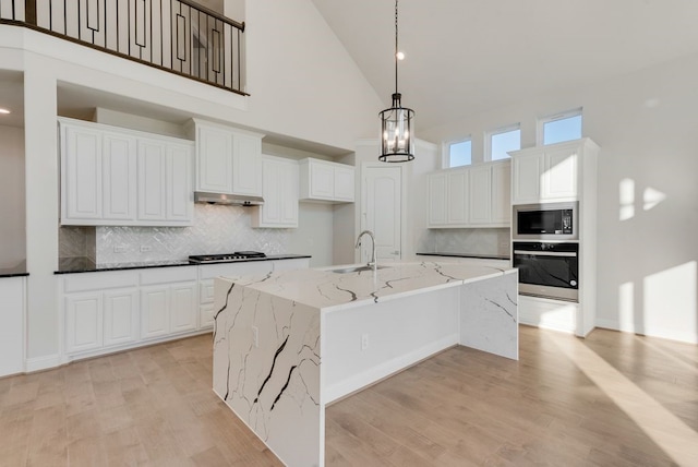 kitchen featuring white cabinets, a kitchen island with sink, stainless steel appliances, and high vaulted ceiling