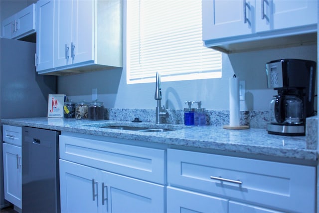 kitchen featuring light stone countertops, sink, stainless steel dishwasher, and white cabinets