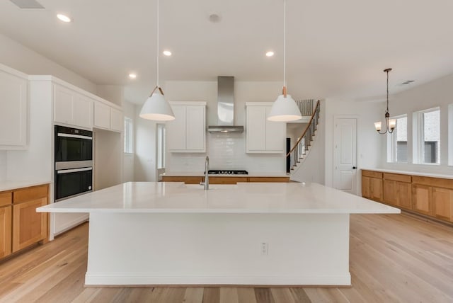 kitchen featuring dobule oven black, light countertops, wall chimney range hood, light wood-type flooring, and decorative backsplash