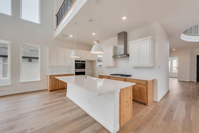 kitchen featuring gas stovetop, light countertops, double oven, a sink, and wall chimney exhaust hood