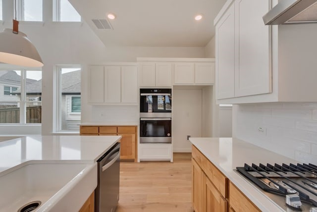 kitchen featuring range hood, light wood finished floors, light countertops, visible vents, and appliances with stainless steel finishes