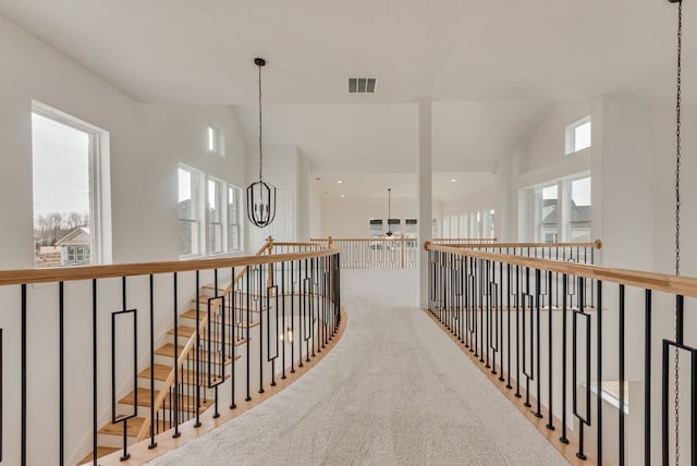 hallway with an inviting chandelier, plenty of natural light, visible vents, and vaulted ceiling