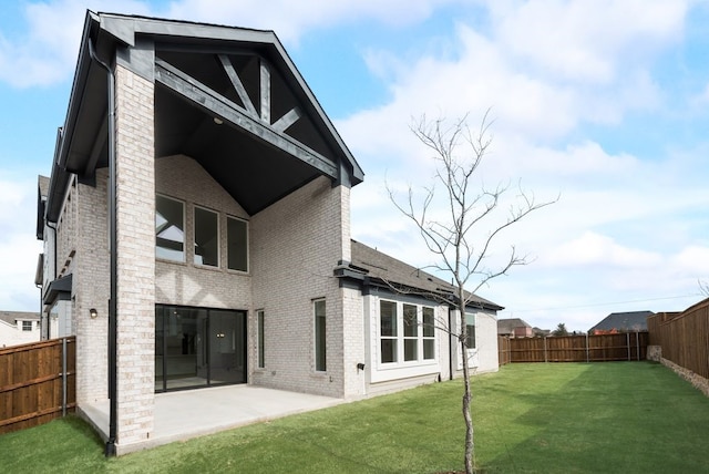 rear view of property with a yard, brick siding, a patio area, and a fenced backyard