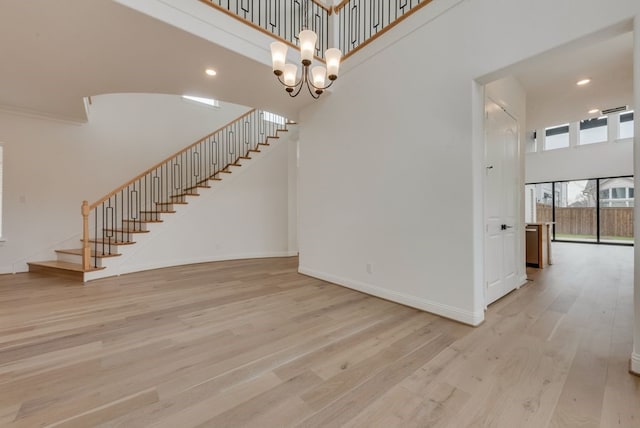 interior space with stairs, light wood finished floors, a towering ceiling, and baseboards